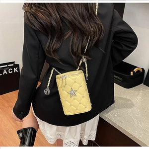 Detail of yellow quilted cylinder mini bag with star rhinestones and chain strap on model