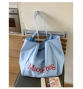 Détail d'un sac cabas en toile bleu clair avec texte rouge posé sur une chaise chez soi