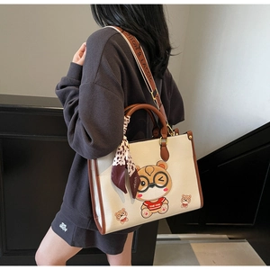 Detail of a large beige tote bag featuring a cartoon bear print and leopard print scarf