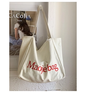 Détail d'un grand sac cabas en toile crème avec impression de lettres rouges sur le mur