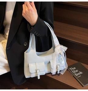 Dettaglio borsa sottobraccio azzurra con fiocco in pizzo bianco e tasche con fibbia