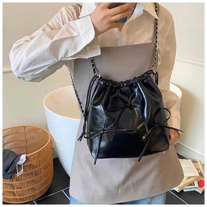 Close-up of black bucket bag featuring glossy leather texture and stylish bow accents