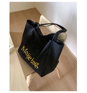 Gros plan sur la broderie jaune Margie Bag d'un sac cabas en toile noire, décor minimaliste