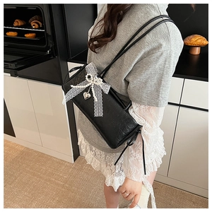 Détail du sac sous l'aisselle noir avec noeud en dentelle blanche et pendentif coeur argenté