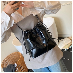 Detail of black drawstring bucket bag featuring leather bows and a silver chain strap
