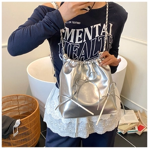Detail of silver metallic bucket bag with ribbon bows and chain straps shown on a model