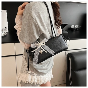Détail du sac à bandoulière noir brillant avec nœud en dentelle, perles et pendentif cœur