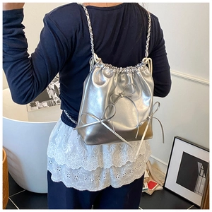 Detail of silver metallic backpack with drawstring closure and bow accents on a model
