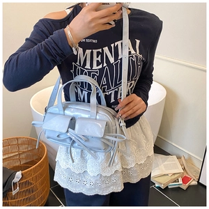 Détail du sac à bandoulière bleu métallisé avec nœuds décoratifs et poches frontales