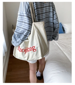 Vue détaillée du sac cabas en toile blanc cassé avec lettrage Maojibag rouge à l'épaule