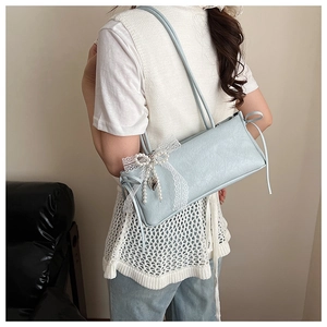 Détail du sac bandoulière bleu clair avec nœud en dentelle et perles porté par un modèle