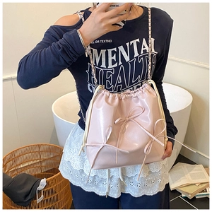 Close-up of pink faux leather bucket bag featuring decorative bows and gold chain strap