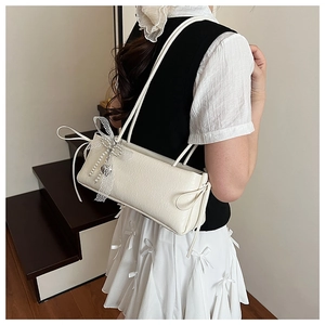 Détail d'un sac en cuir gaufré crème avec nœud en dentelle et pendentif cœur perlé