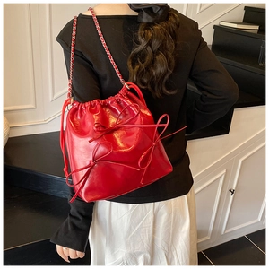 Detail of red glossy bucket bag featuring handcrafted bows and gold-tone chain strap