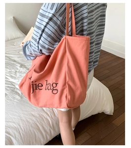 Détail du sac cabas en toile orange corail avec imprimé noir porté par un mannequin