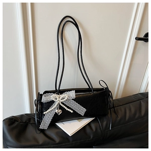 Détail du sac à bandoulière noir avec nœud en dentelle blanche et pendentif cœur perlé