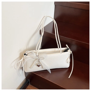 Détail du sac crème avec nœud en dentelle, chaîne de perles et pendentif cœur argenté