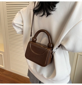 Détail d'un sac carré marron brillant avec poignée ronde et boucles en argent