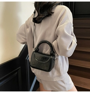 Détail d'un sac à main noir brillant avec poignée ronde et accents de sphères chromées