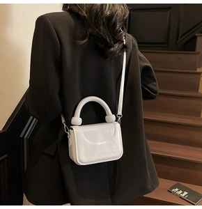 Sac boîte blanc chic avec poignée ronde porté par un mannequin en blazer noir élégant