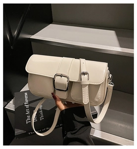Close-up of minimalist beige shoulder bag featuring dual silver buckles and smooth leather