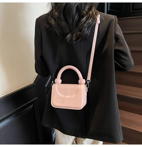 Sac bandoulière en cuir verni rose porté par un mannequin dans un escalier moderne