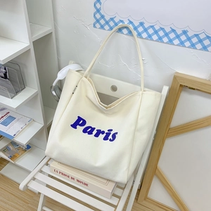 Detalle de bolso tote de lona blanco roto con letras Paris en azul sobre silla blanca