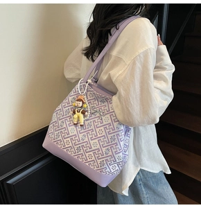 Detail of a purple patterned tote bag featuring a metallic bow and cartoon charm