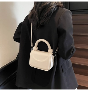 Détail d'un sac à main blanc crème avec une poignée ronde et des accents de sphère