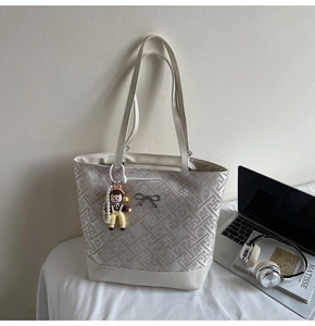 Close-up of beige tote bag with floral patterns, metal bow, and cartoon girl charm
