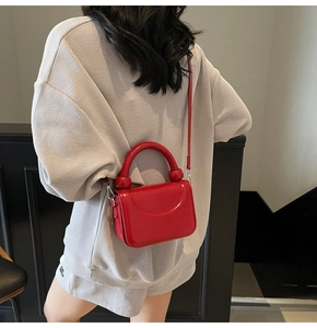 Modèle portant un sac bandoulière en cuir verni rouge avec poignée incurvée et breloques