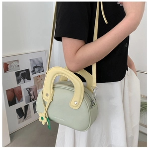 Gros plan du sac à main vert pastel en cuir grainé avec poignée jaune et breloque fleur
