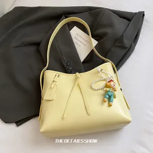 Detail view of yellow faux leather tote with pearl charm and cartoon doll accessory