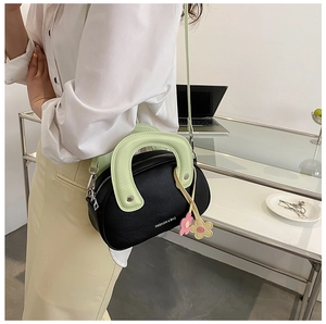 Détail du petit sac bandoulière noir avec poignée verte et breloque fleur sur un bureau