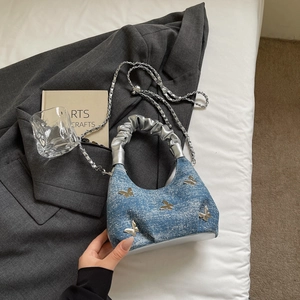 Detail of blue denim butterfly handbag with silver chain on a grey blazer background
