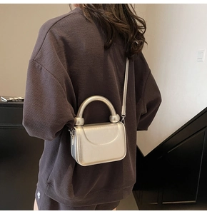 Mini sac carré métallisé argenté avec poignée épaisse porté en bandoulière par le mannequin