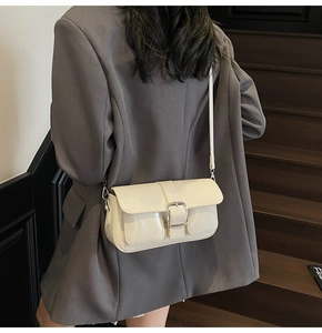 Model wearing a minimalist cream patent leather underarm bag with metal buckle closure