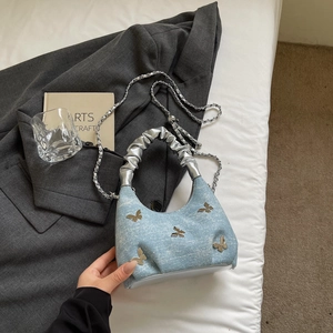 Detail of light blue denim underarm bag with silver butterfly and metallic cloud handle