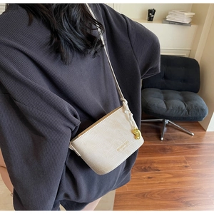 Détail du sac seau crème avec texture crocodile et breloque dorée porté par un mannequin