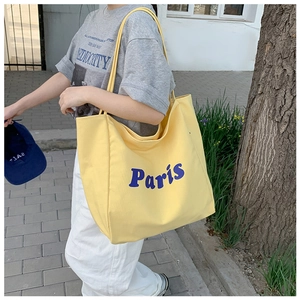 Primer plano de un bolso tote de lona amarilla con letras de París en un entorno de calle