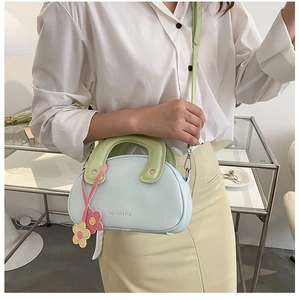 Détail d'un sac à main bleu clair avec poignée vert pastel et breloque florale