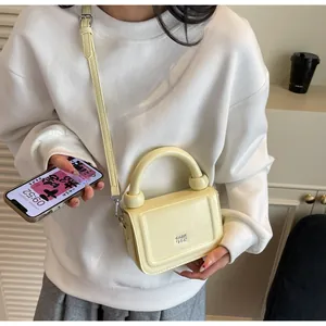 Petit sac carré jaune crème porté par un mannequin dans un intérieur au style épuré