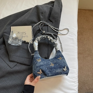 Detail of blue denim hobo bag featuring silver butterfly motifs and metal chain strap