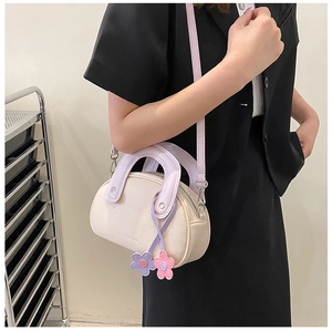 Détail du sac crème avec poignées lilas et breloques fleurs sur une veste noire
