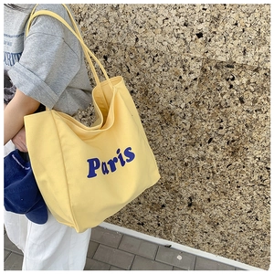 Detalle de un bolso tote grande de lona amarilla con letras Paris azules impresas