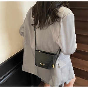 Sac seau noir chic à motif crocodile porté avec un blazer gris sur un escalier