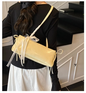 Détail du sac baguette crème avec un nœud en dentelle blanche et de longs glands sur le dos