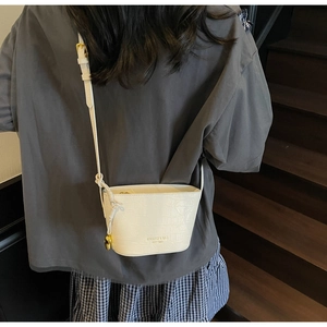 Détail d'un mini sac seau blanc à motif crocodile avec logo doré et breloque cœur