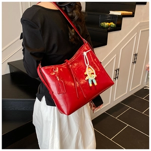 Detail view of a bright red glossy leather tote bag with stylish cartoon pendant ornament
