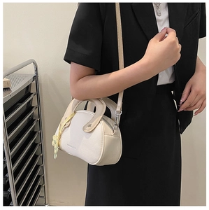 Détail du sac à bandoulière crème avec texture litchi, breloque fleur et boucle